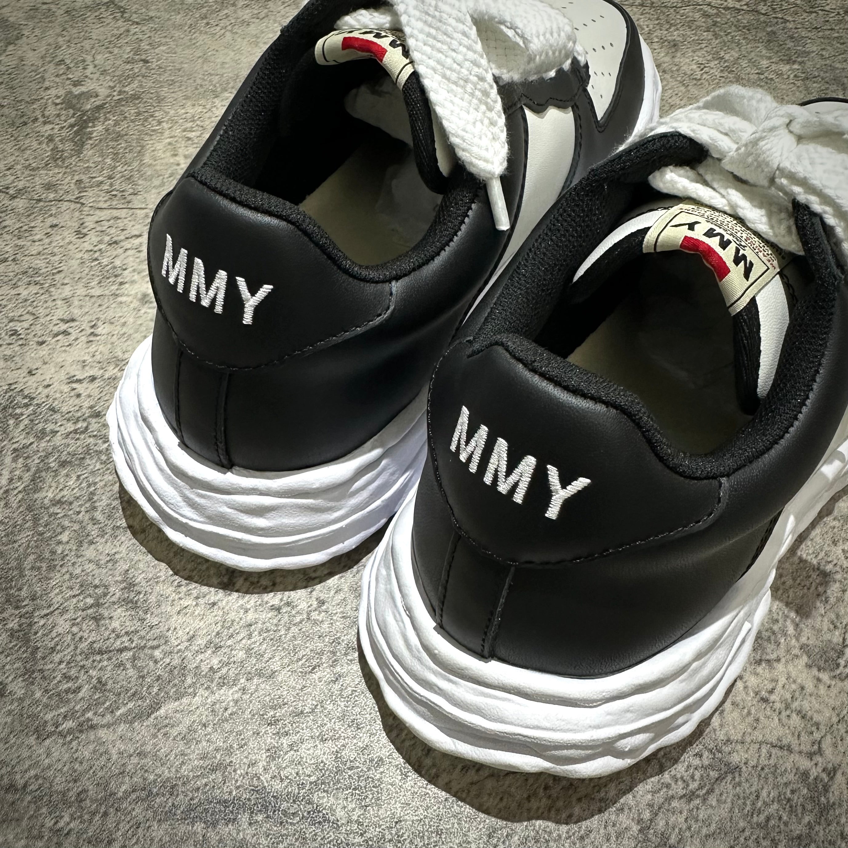 Close-up of MMY WAYNE OG Leather shoes in black and white showing the back detail with MMY branding.