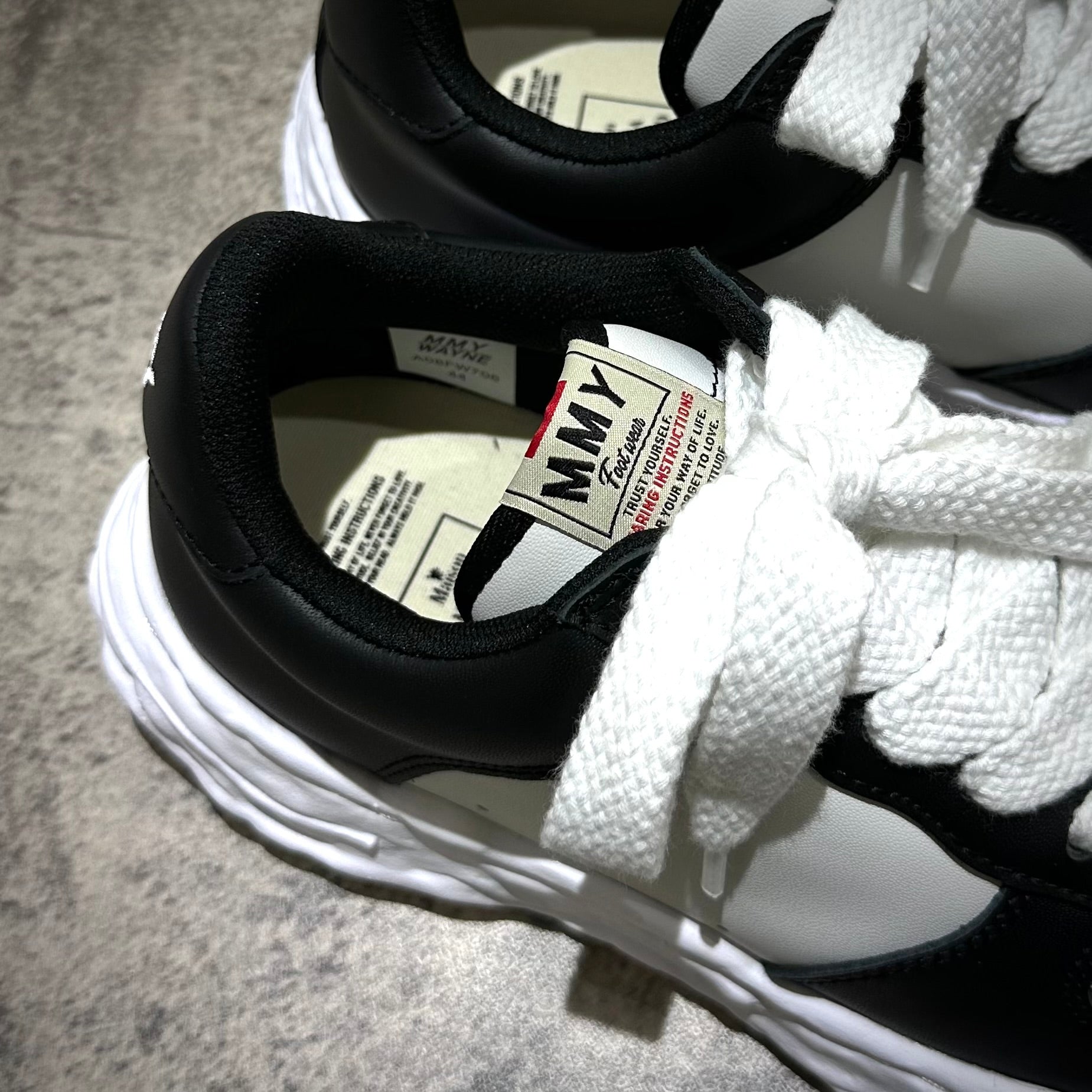 Close-up of MMY WAYNE OG Leather black and white sneakers with lace details.