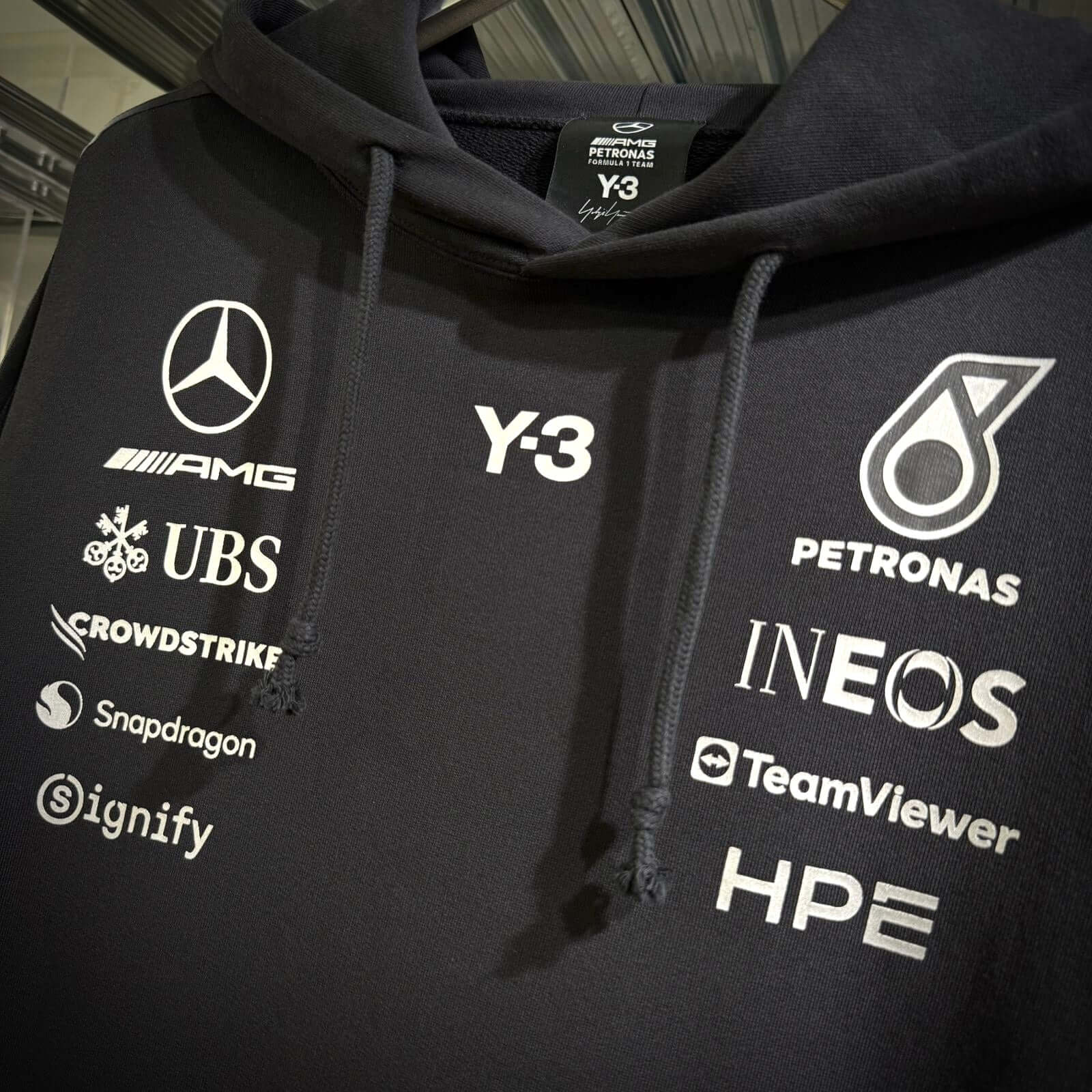 Y-3 x Mercedes AMG Petronas F1 Hoodie showcasing logos on a black fabric background.