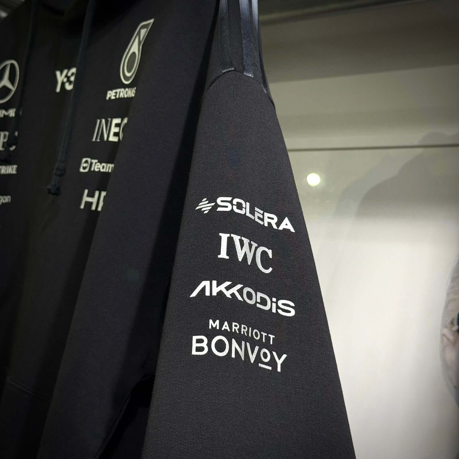 Close-up of the sleeve of Y-3 x Mercedes AMG Petronas F1 Hoodie featuring sponsor logos on a black background.