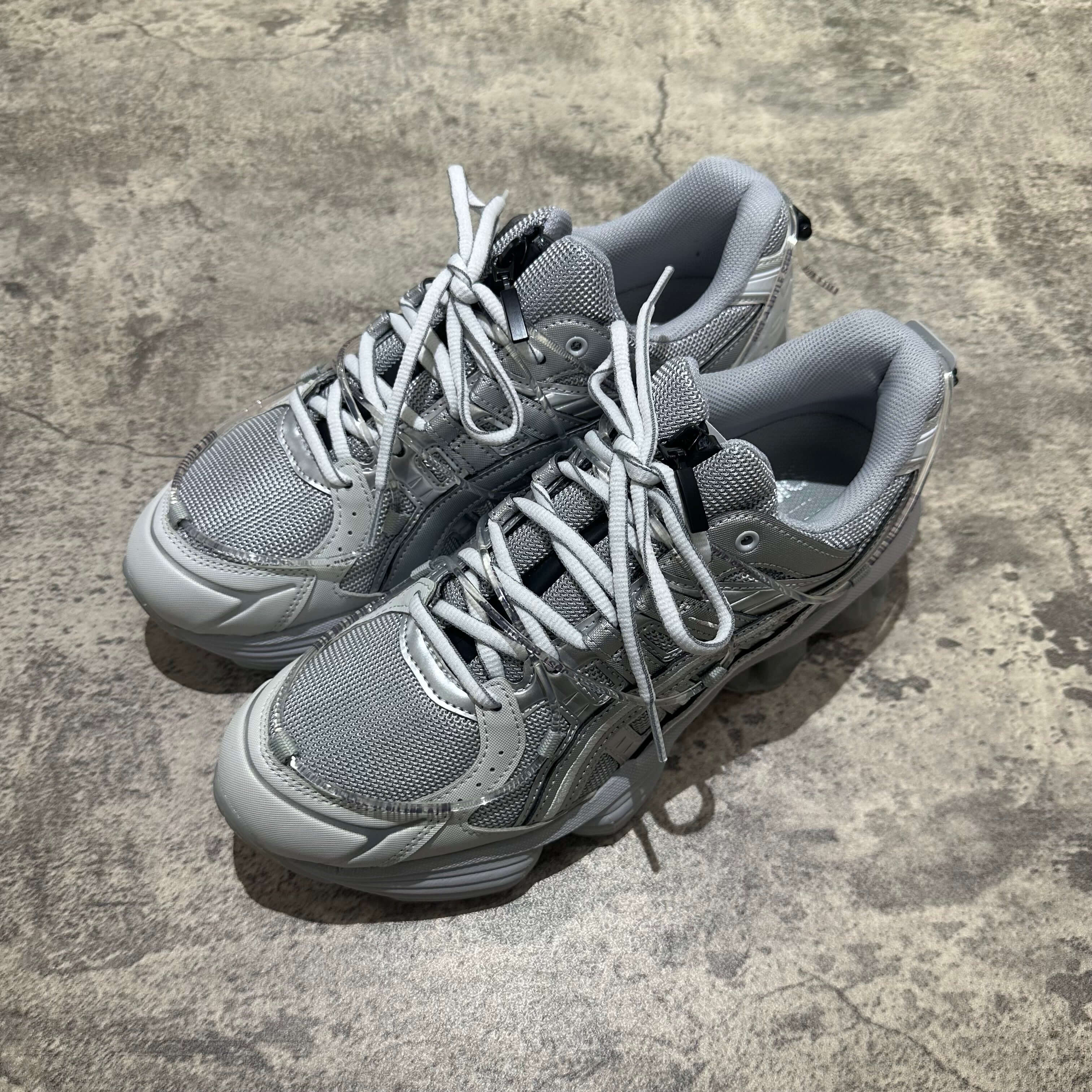 Yoasobi x Asics Gel Kinetic Fluent Y in Piedmont Grey and Pure Silver with laces on a textured surface.