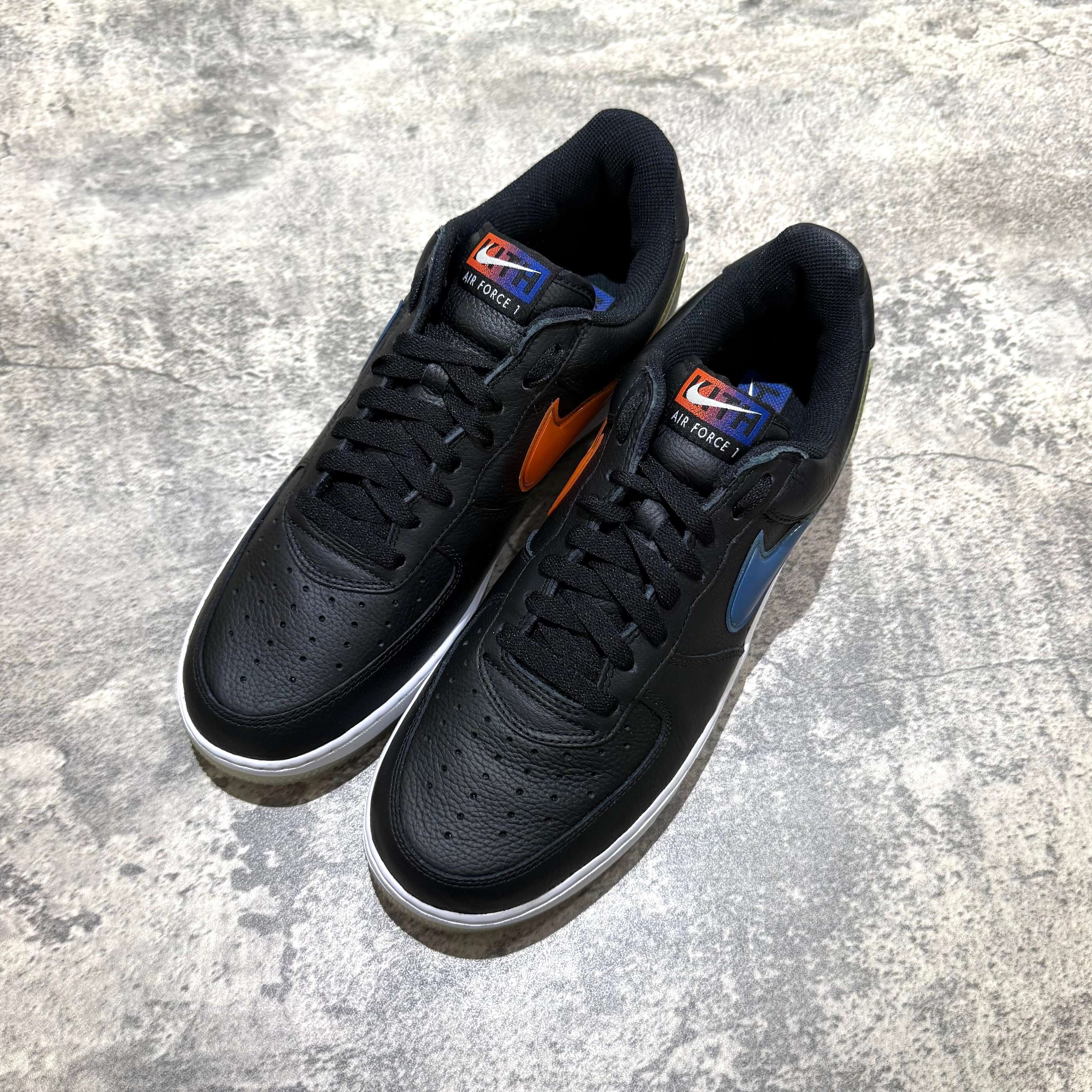 KITH x Nike Air Force 1 Low Knicks black sneakers with orange and blue accents on a gray background.