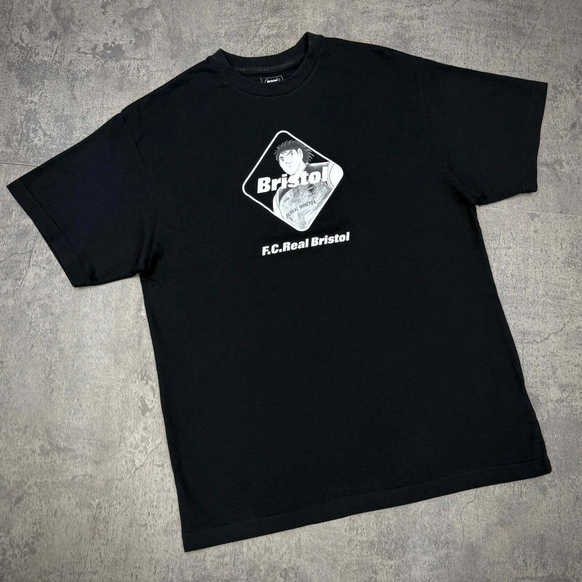 Kojiro Hyuga x F.C.Real Bristol Emblem Tee showcasing a stylish design on a black t-shirt with vintage anime influence.