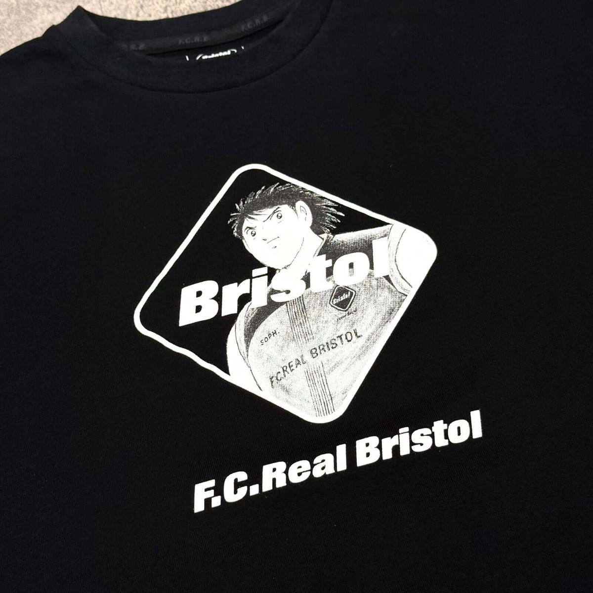 Kojiro Hyuga x F.C.Real Bristol Emblem Tee featuring the vintage anime design on a black shirt.