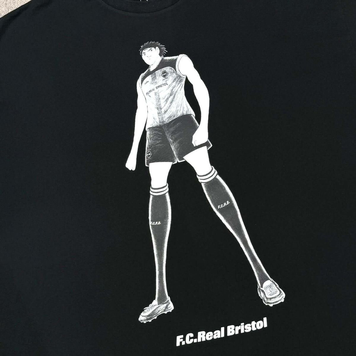 Kojiro Hyuga x F.C.Real Bristol On The Front Baggy Tee black illustration of a character with F.C.Real Bristol logo