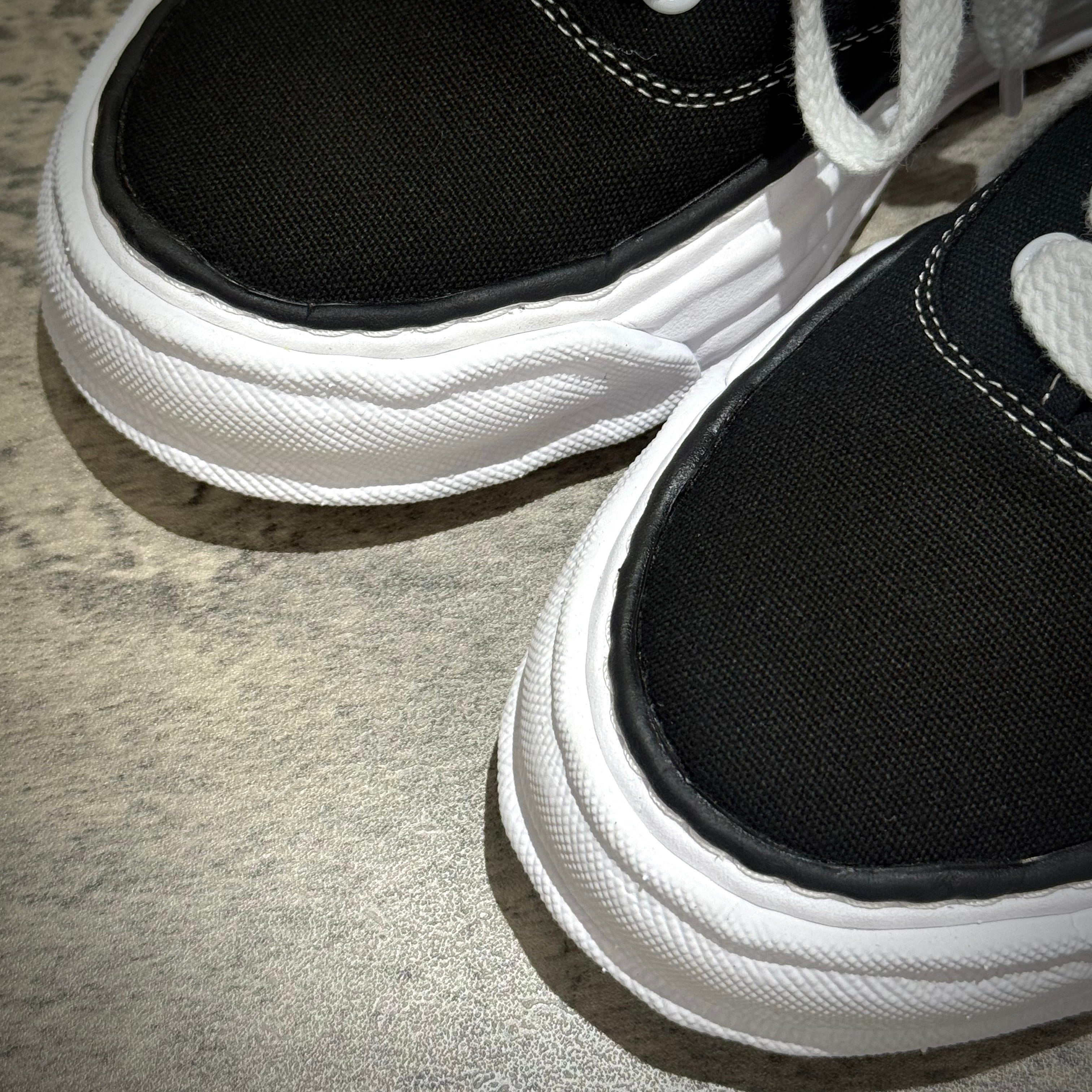 Close-up of MMY Baker26 Canvas Low - Black sneakers showing black canvas upper and white sole details.
