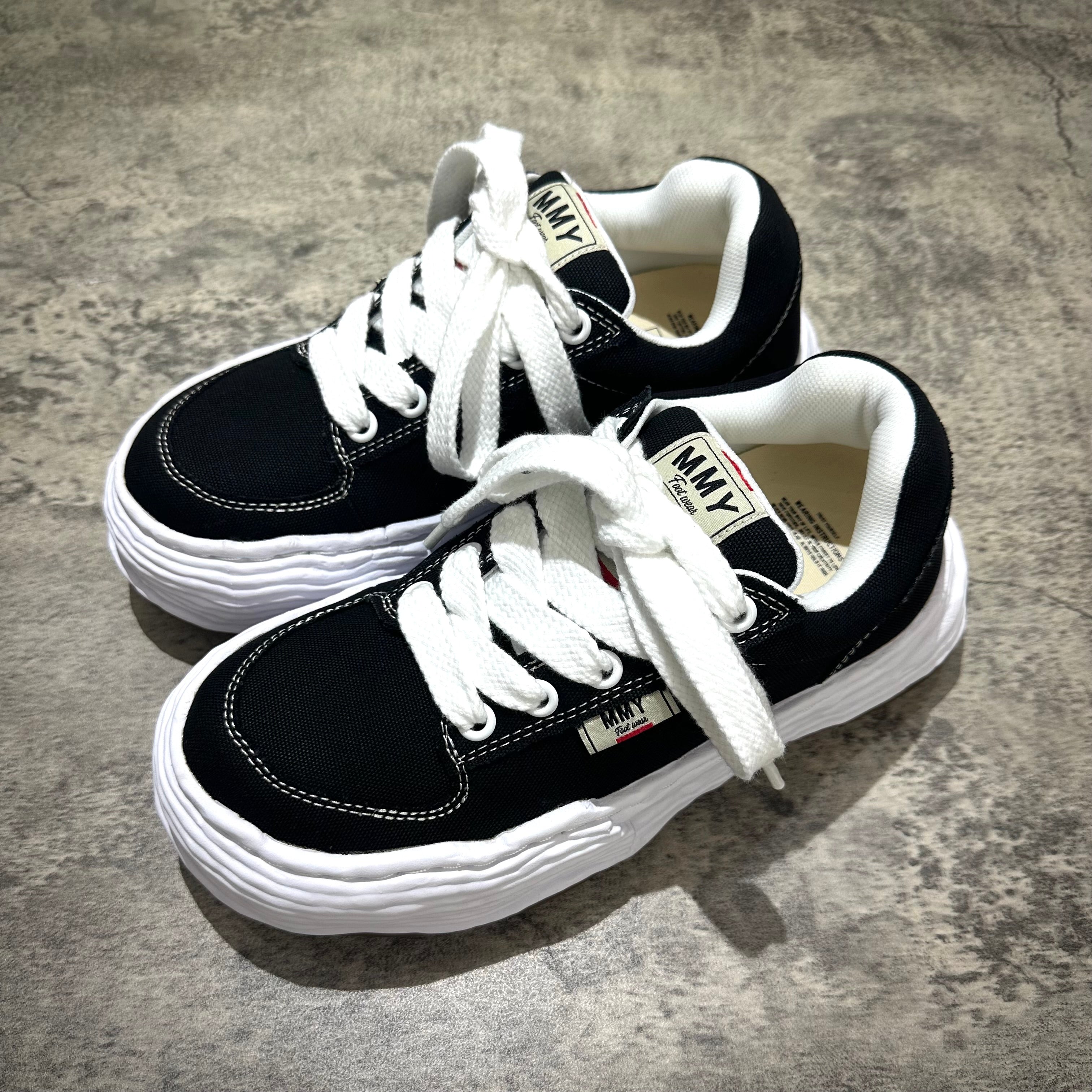 MMY Oliver Canvas Low - Black sneakers with white laces on a grey background.