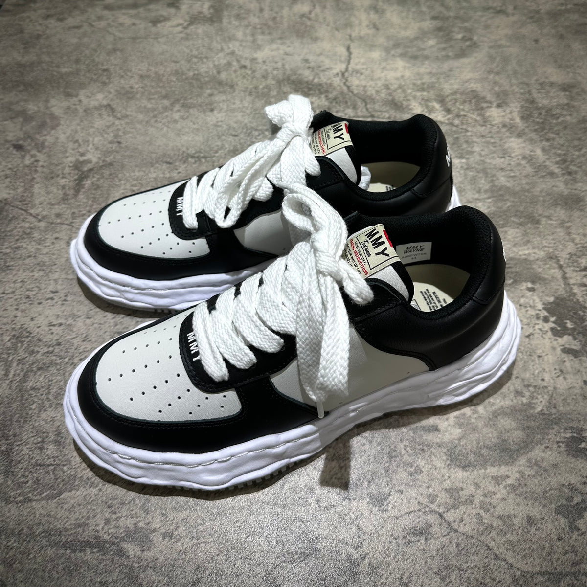 MMY WAYNE OG Leather sneaker in black and white with lace-up design on a gray surface.