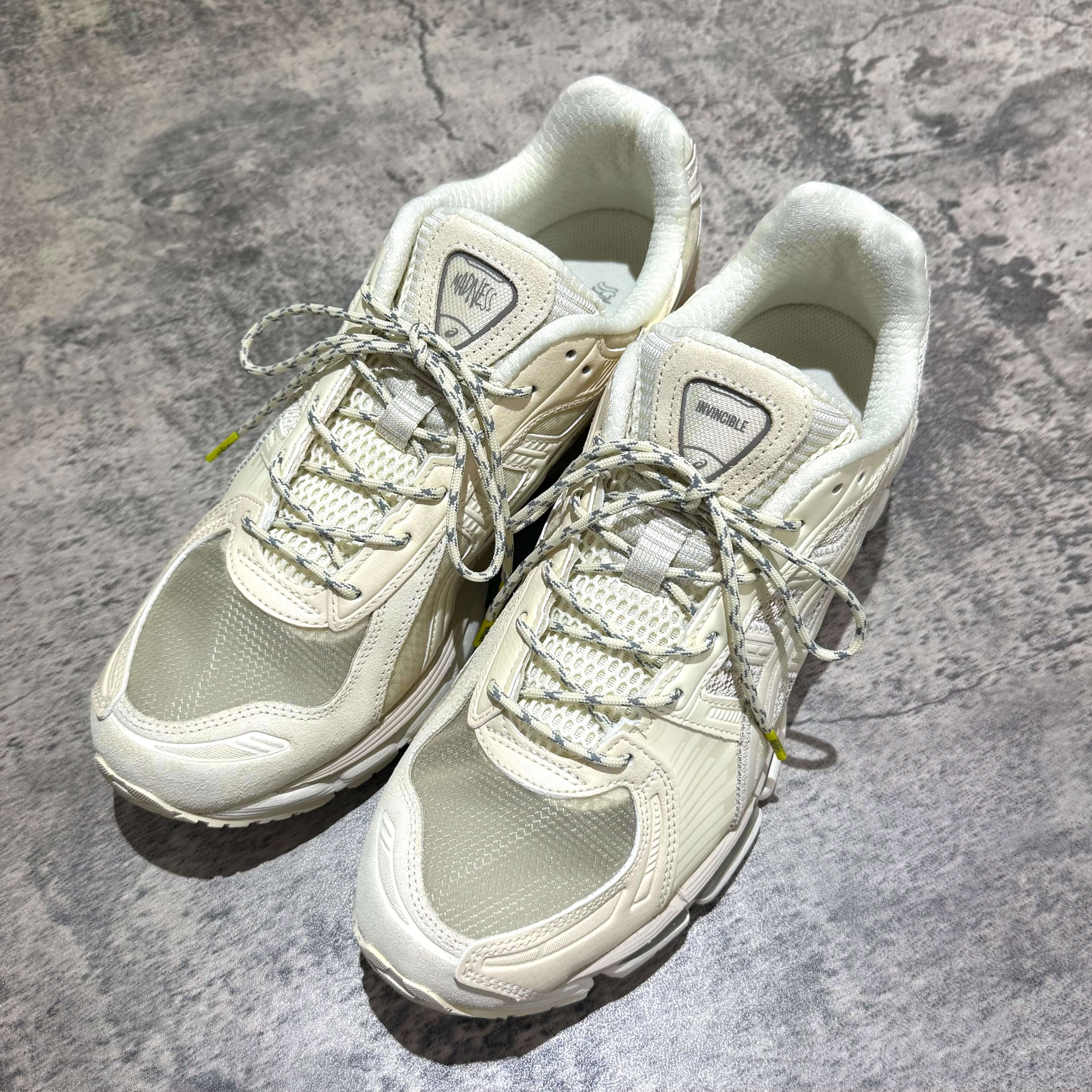 Madness x Invincible x Asics Gel-Kayano 12.1 Vanilla shoes displayed from above on a textured surface.