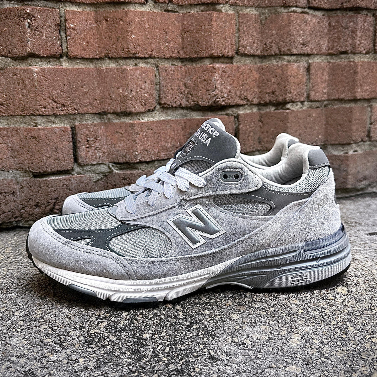 New Balance Made in USA 993 Grey sneakers on a textured surface with a brick background.