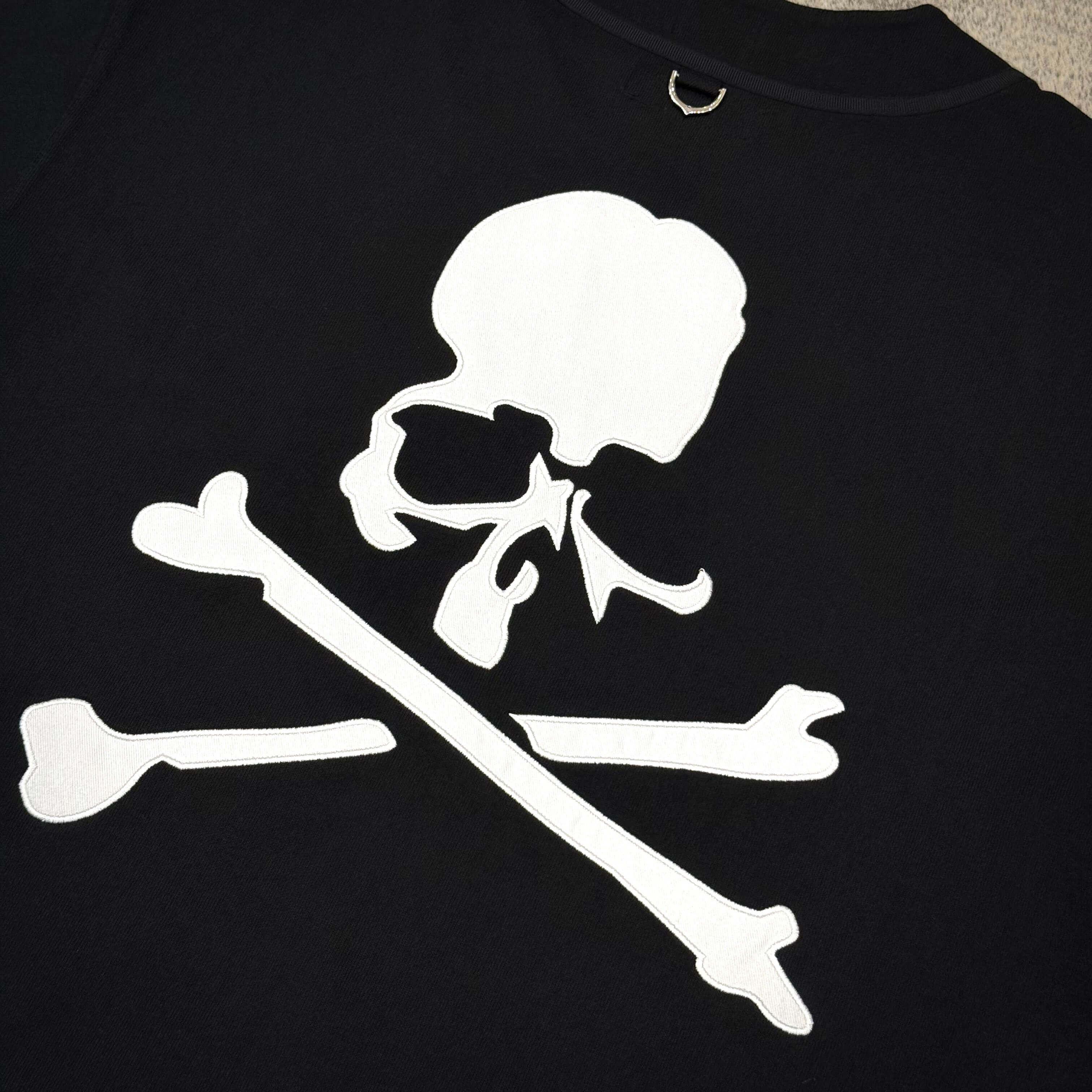 Skull and crossbones logo design in white on a black background, featured on apparel.