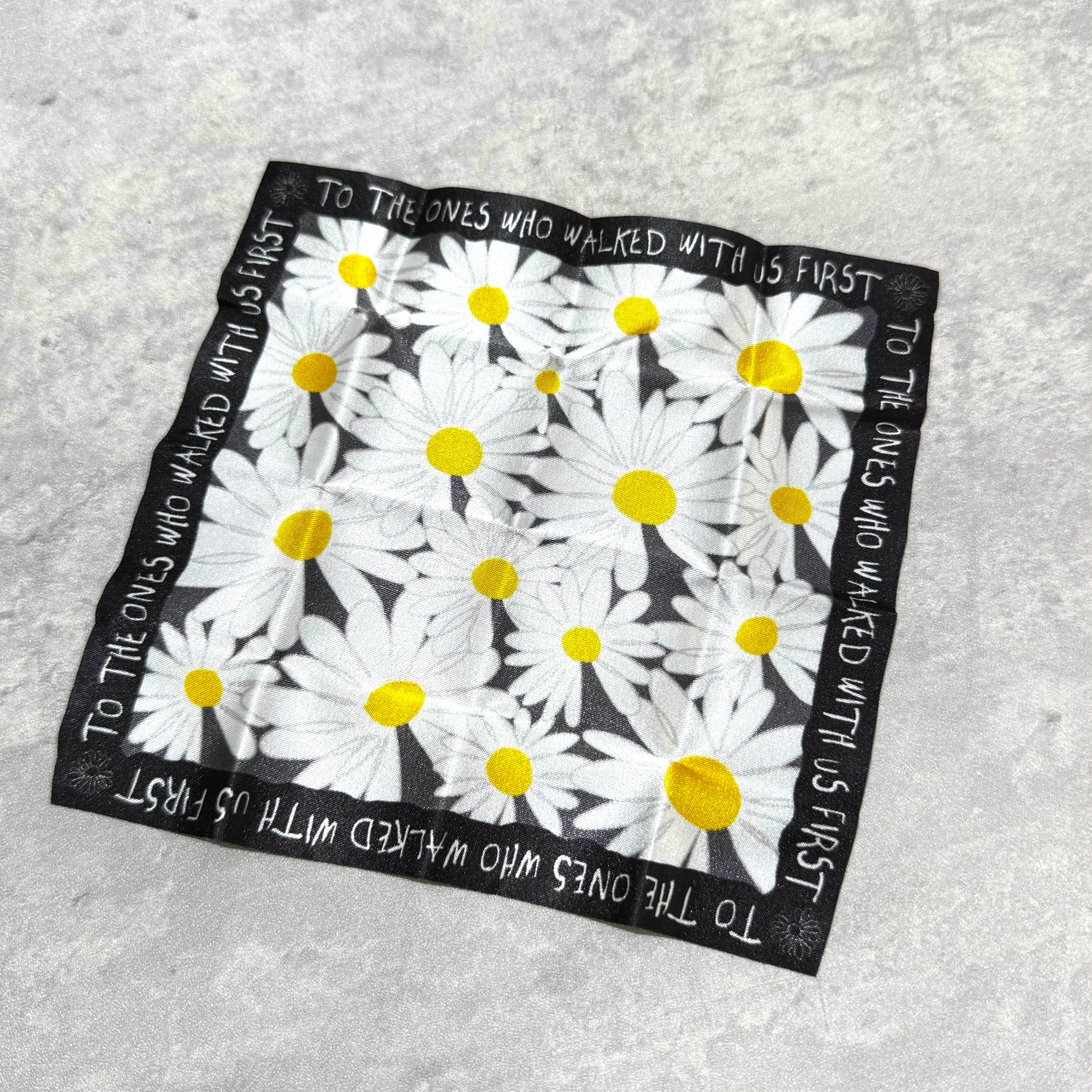 Daisy patterned square scarf with yellow dots and text saying 'To the ones who walked with us first'.