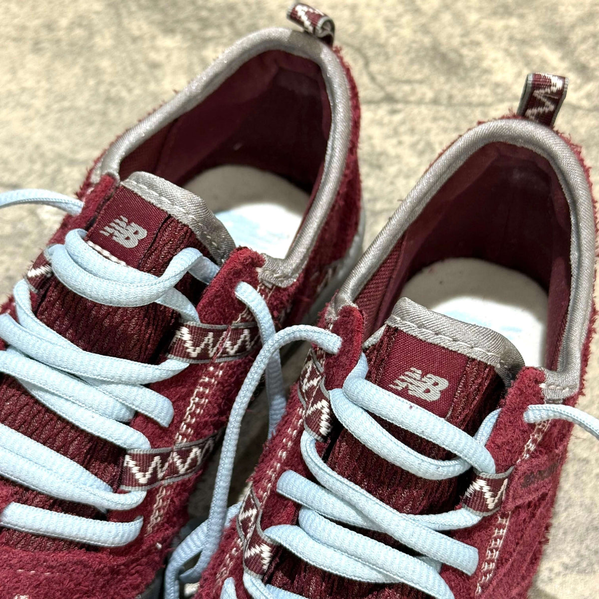 SUNLOVETOUR x New Balance MT1001ND close-up view showcasing the burgundy textile upper and light blue laces.