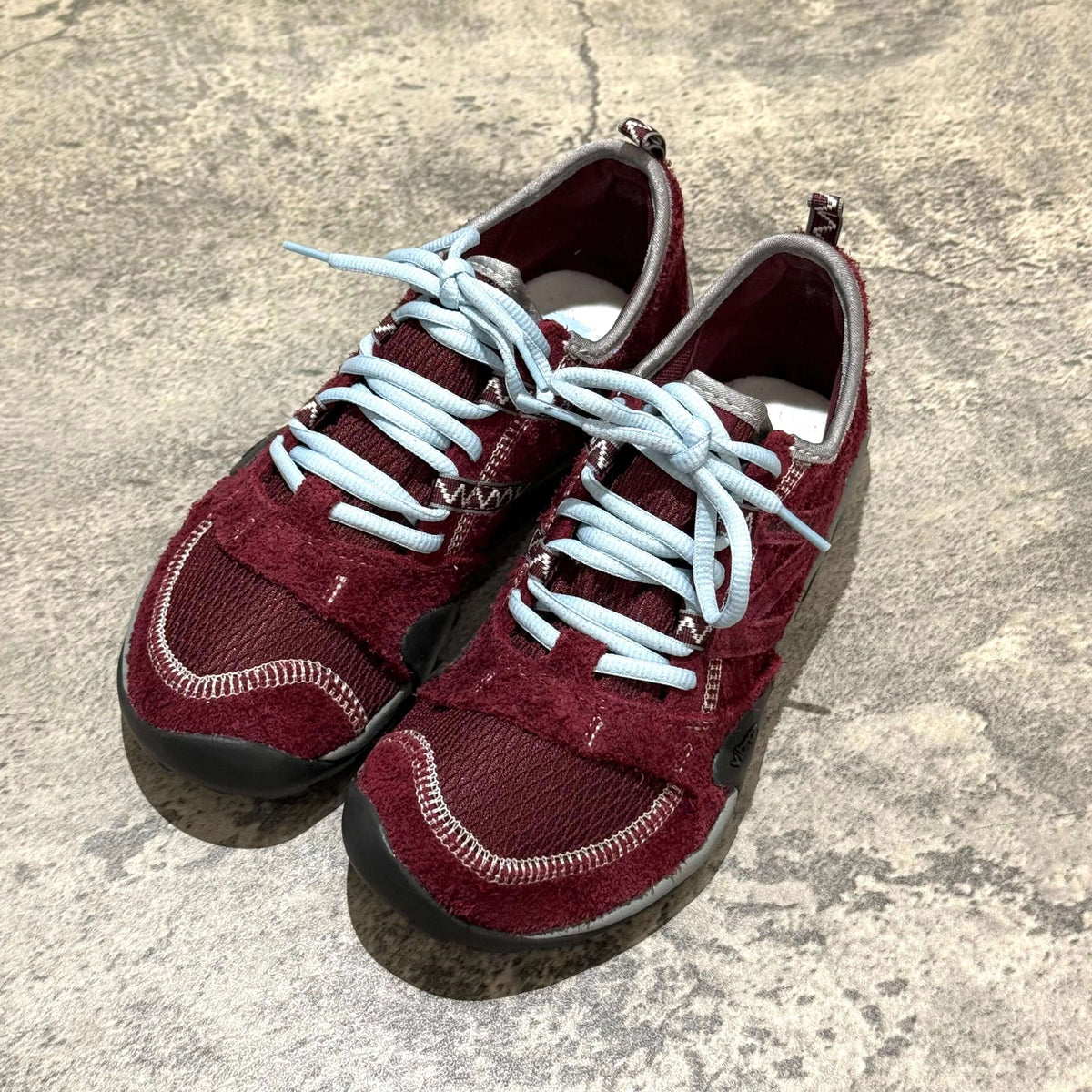 SUNLOVETOUR x New Balance MT1001ND red and gray sneakers with blue laces on a textured surface.