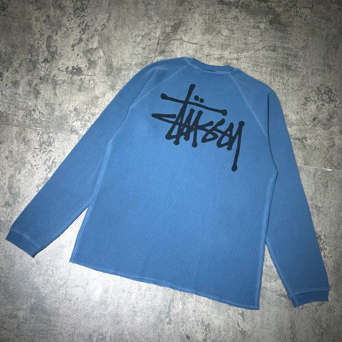 Stussy Basic Raglan Thermal LS Crew FW26 in blue, featuring a black logo on the back, showcasing a stylish casual design.
