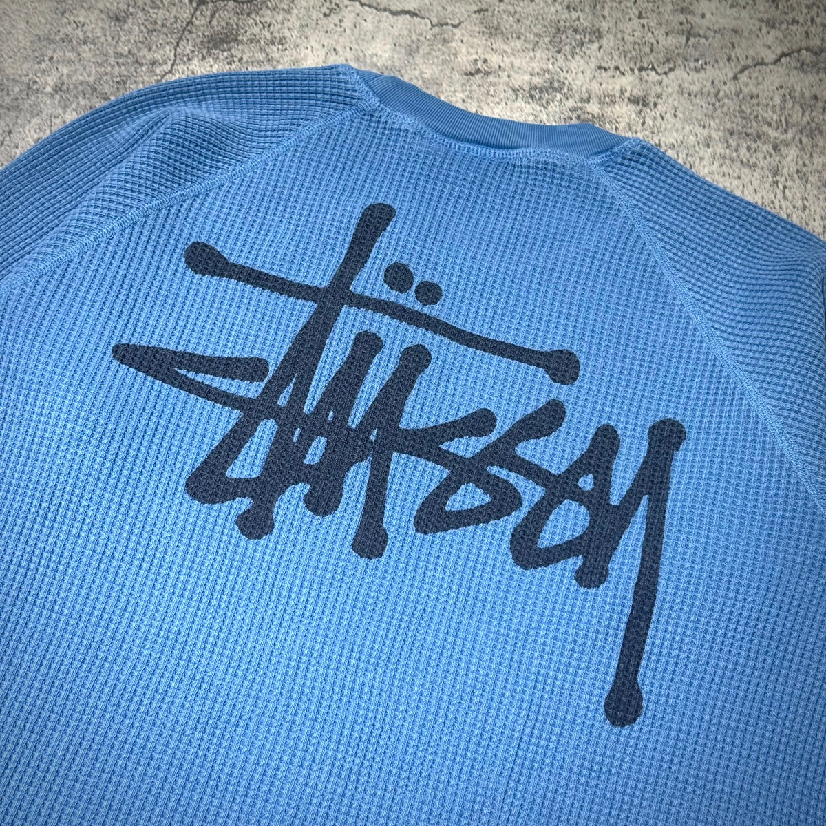 Stussy Basic Raglan Thermal LS Crew FW26 in blue with black logo on the back, showcasing stylish streetwear design.