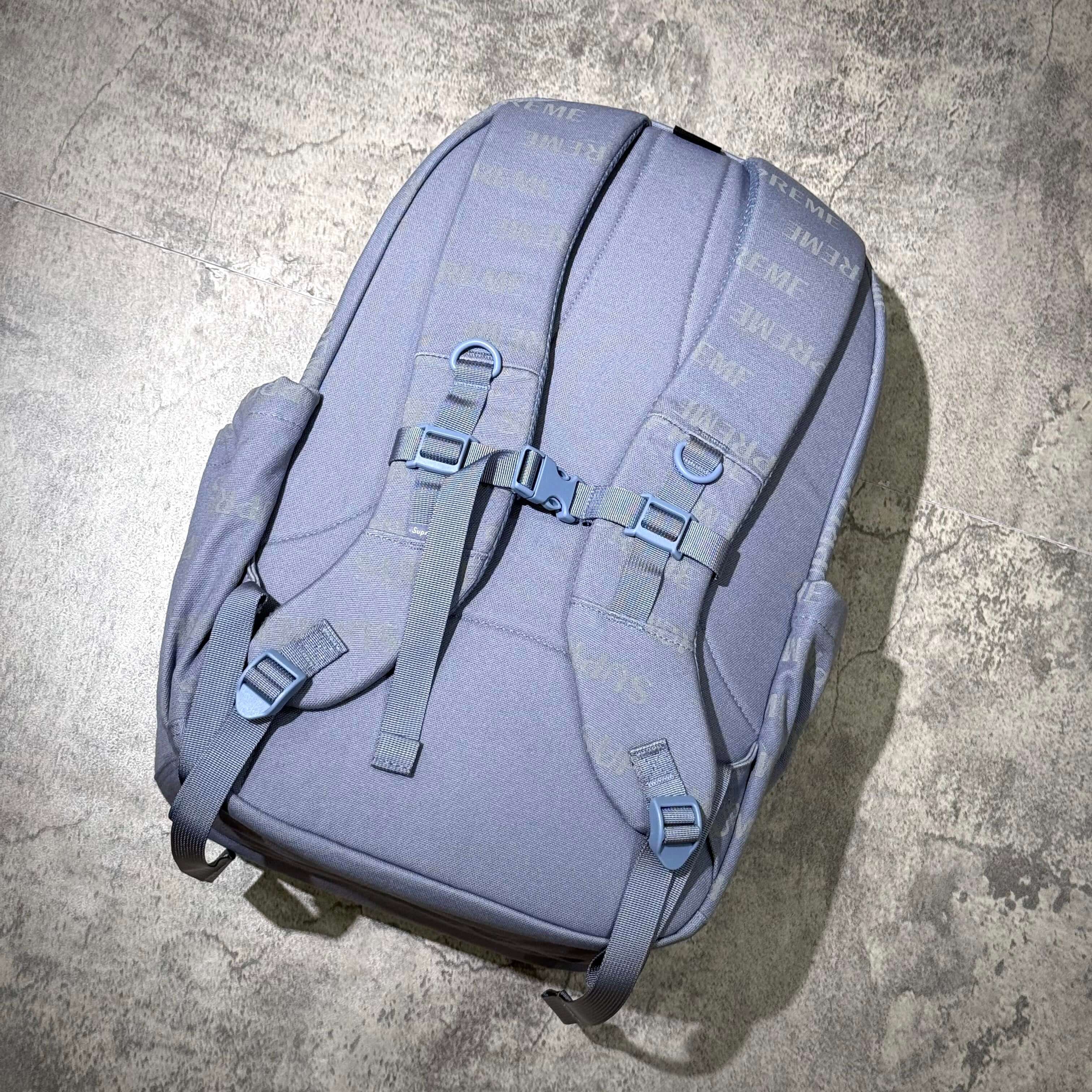 Supreme FW26 Backpack featuring padded straps and a stylish gray design on a textured surface.
