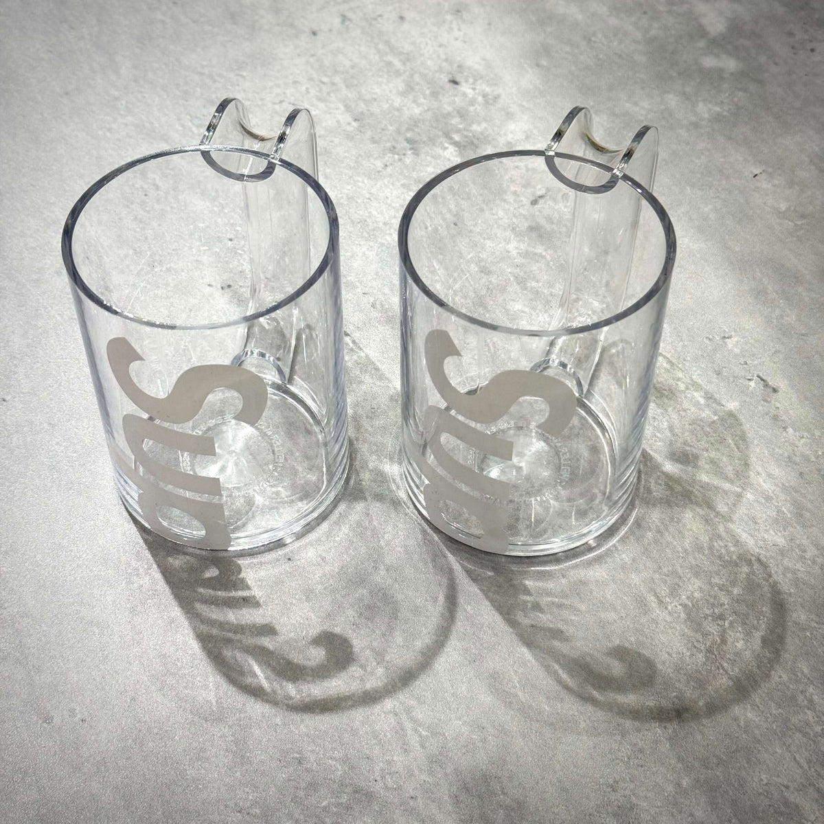 Supreme Heller Mugs Set of 2 - Clear displayed on a surface, showcasing their transparent design and logo.
