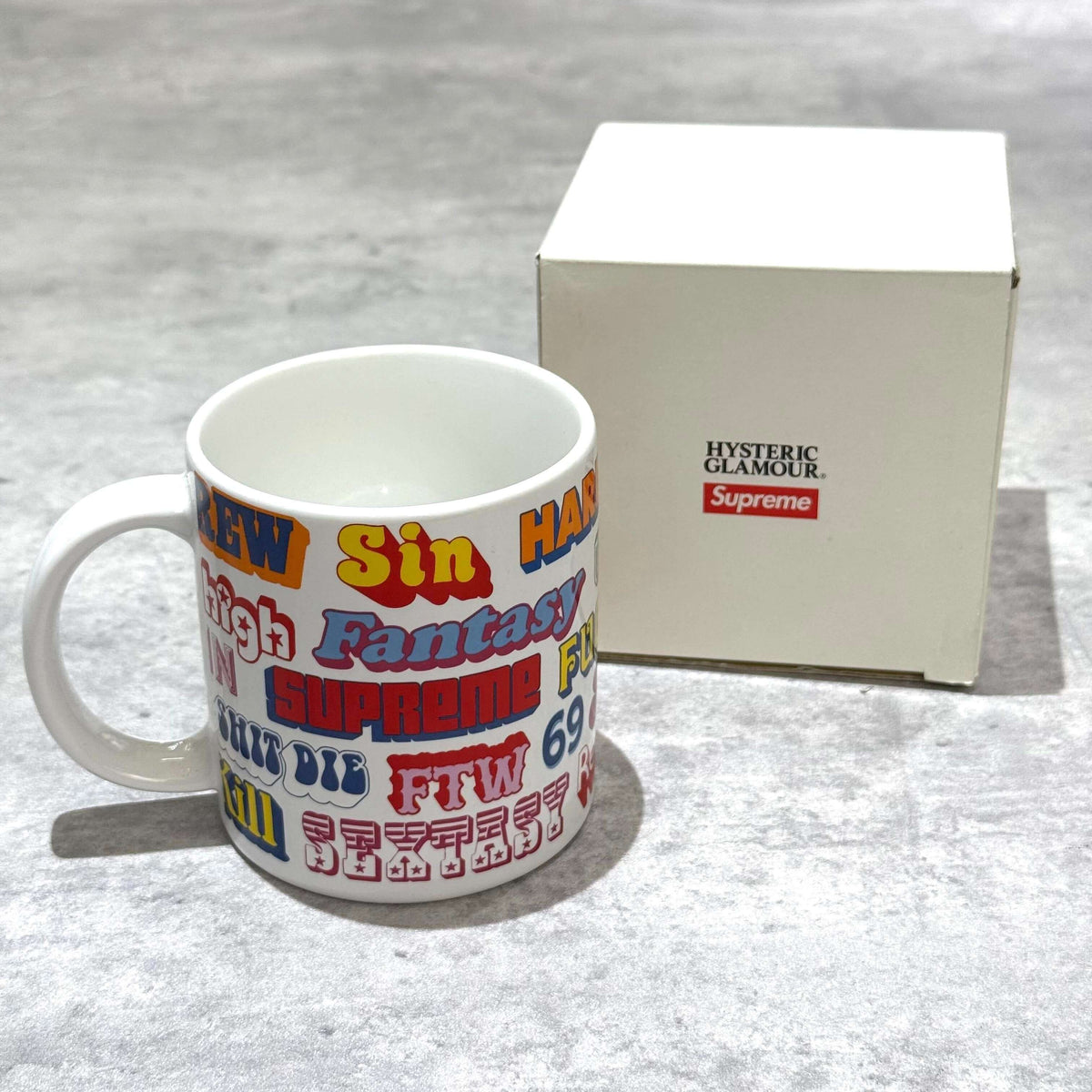 Supreme Hysteric Glamour Ceramic Coffee Mug with colorful logo designs next to its box