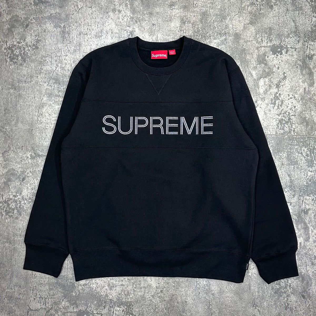 Supreme Zig Zag Stitch Panel Crewneck displayed on a gray surface, featuring a stylish black design with a bold logo.