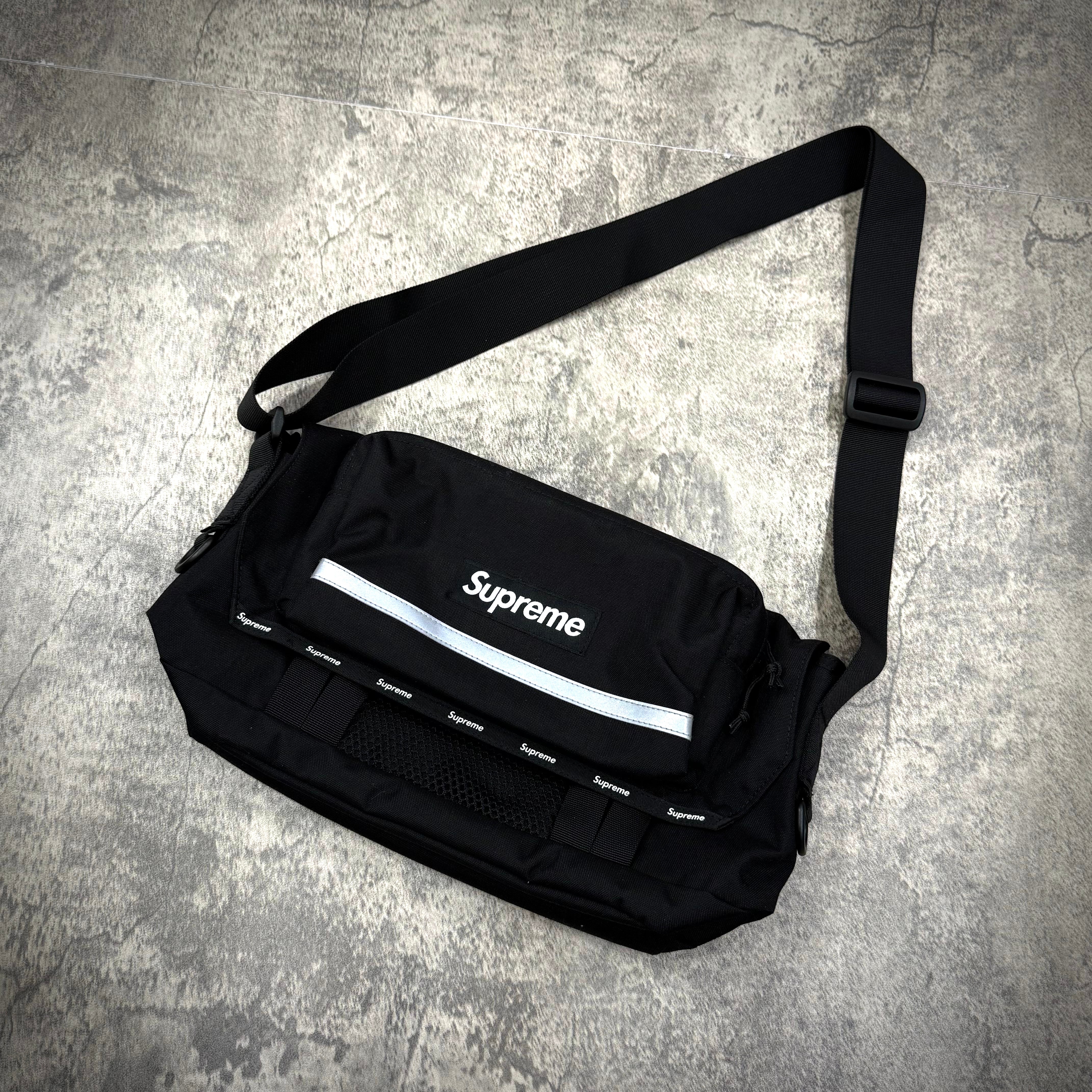 Supreme Messenger Bag FW24 in black with adjustable strap and reflective stripe, showcasing embossed logo and multiple pockets.