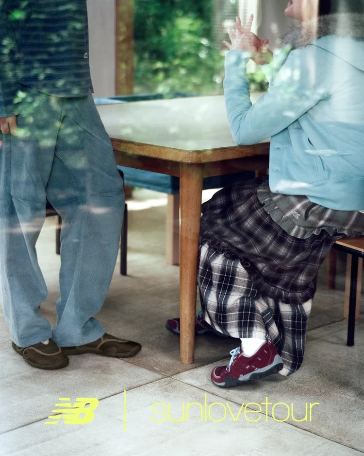 Two individuals wearing SUNLOVETOUR x New Blance MT1001ND sneakers sitting at a table in a modern setting.