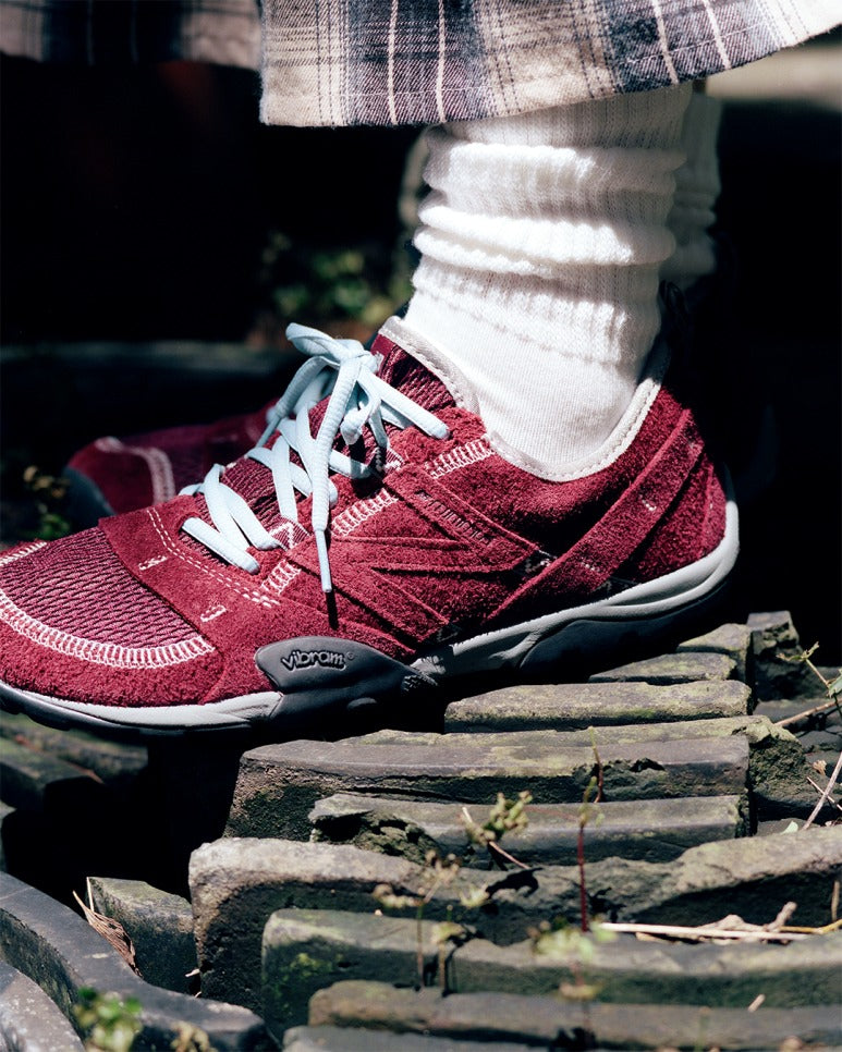 SUNLOVETOUR x New Blance MT1001ND shoes in maroon color on rocky terrain.