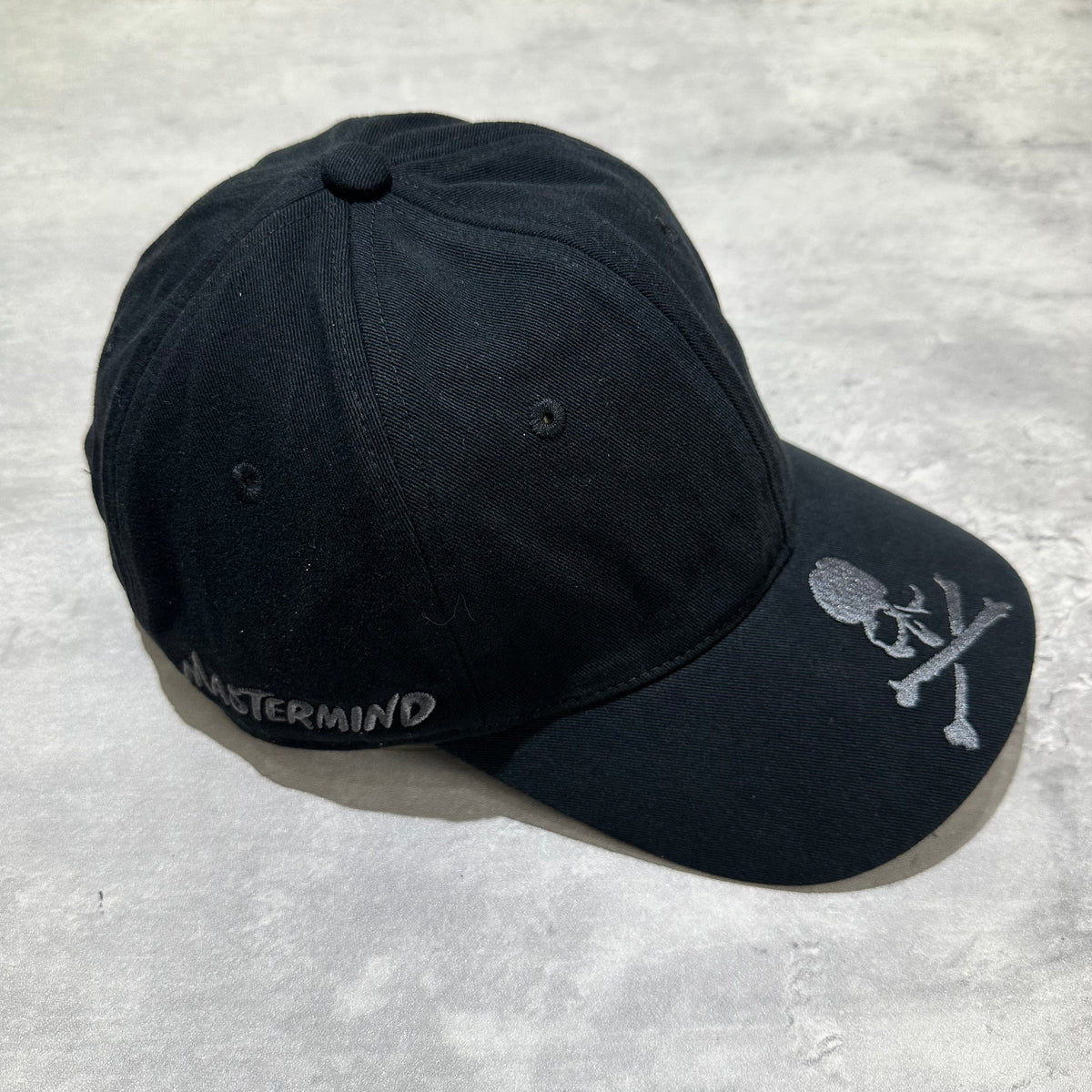 Wild Things x Mastermind World Tee Cap featuring a black design with embroidered skull and text.