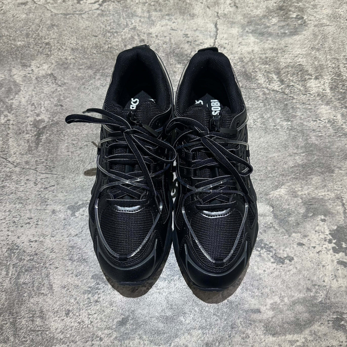 Yoasobi x Asics Gel Kinetic Fluent Y - Black sneakers top view with black mesh and laces on a textured surface.
