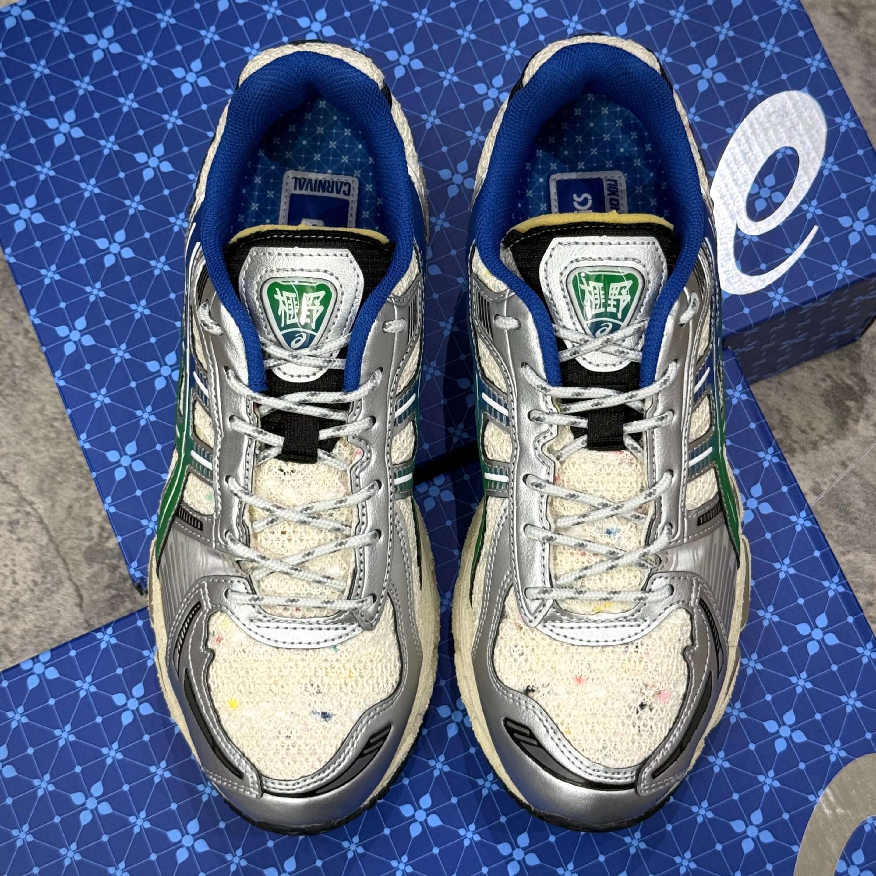 Top view of Carnival x Asics Gel Kayano 12.1 PHRA NAKHON sneakers on a blue patterned background.