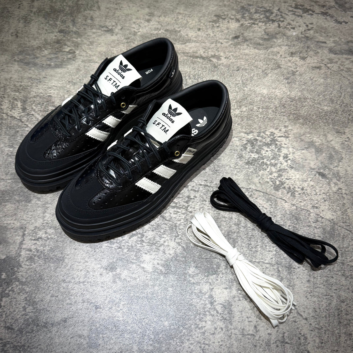 adidas Samba LX Freizeit x Song For The Mute black sneakers with laces on a gray background.