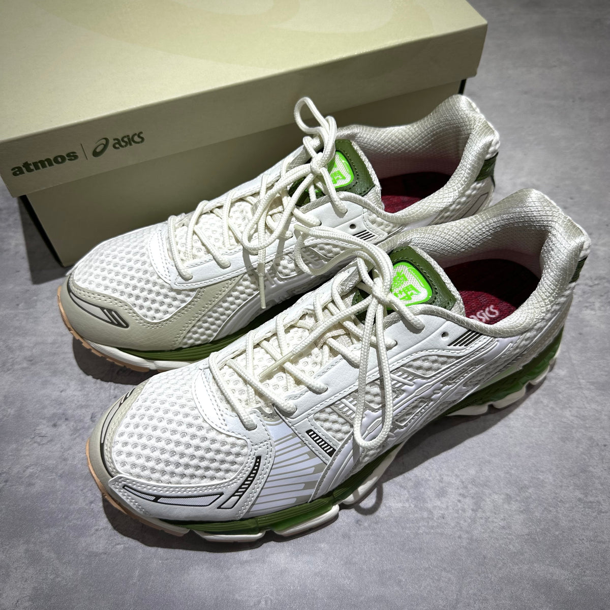 atmos x Asics Gel-Kayano 12.1 Archipelago white and green sneakers on a gray surface with box in background
