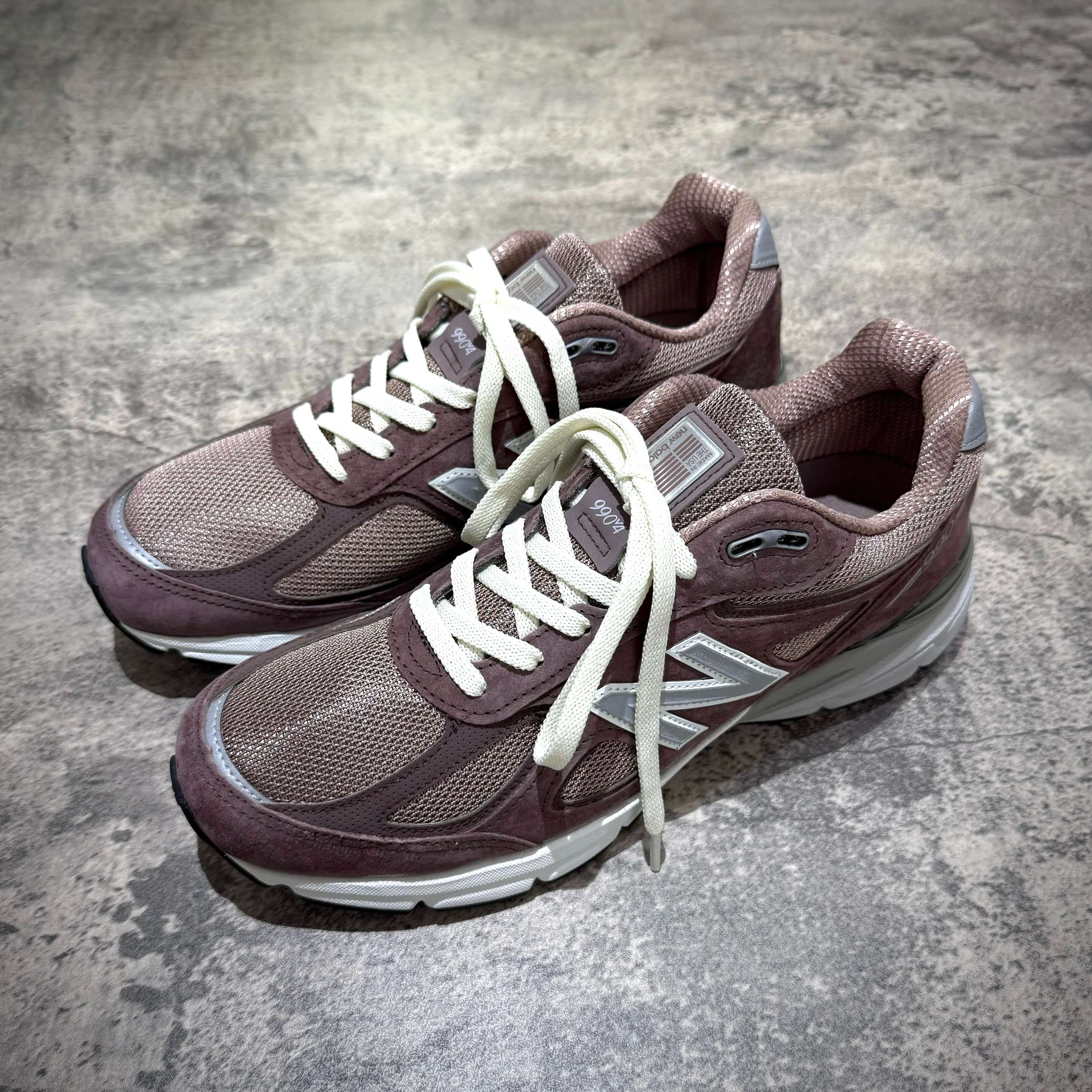 MiUSA Kith x New Balance 990v4 Dusty Mauve sneakers displayed from the top view on a textured surface.