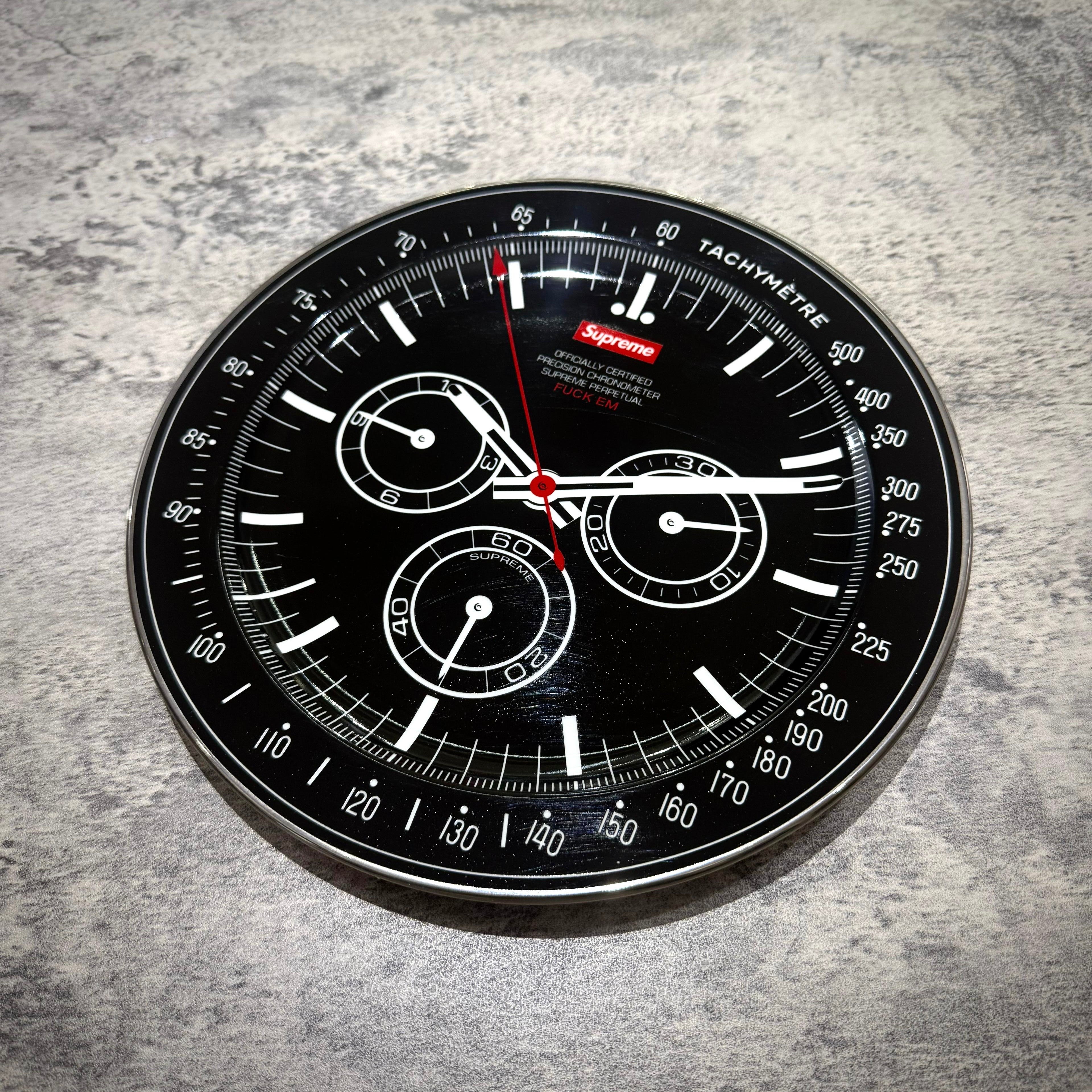 Supreme Watch Plate - Black with tachymetre design and red accents on a textured surface.
