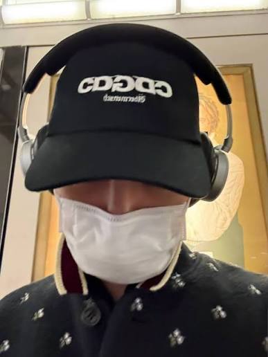 Person wearing a CDG x G-DRAGON Ubermensch Classic Cap with headphones and a mask